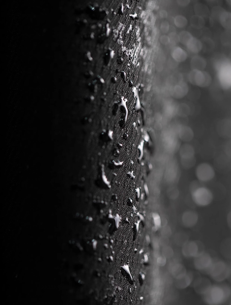 Close-up of water-repellent coated black fabric with droplets.