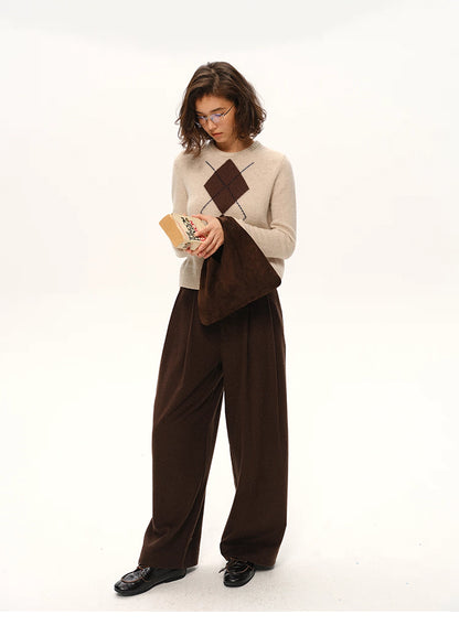 Full body shot of beige argyle wool sweater styled with brown trousers and matching suede bag.