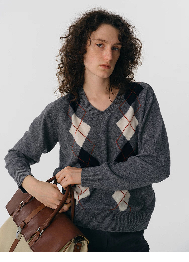 Close-up of charcoal argyle V-neck wool sweater with ivory and black diamonds while holding a leather briefcase.
