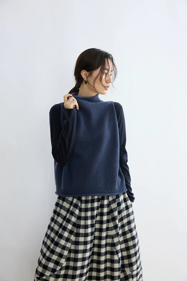 Model touching the rolled mock neck of an Ink Blue cropped wool sweater vest