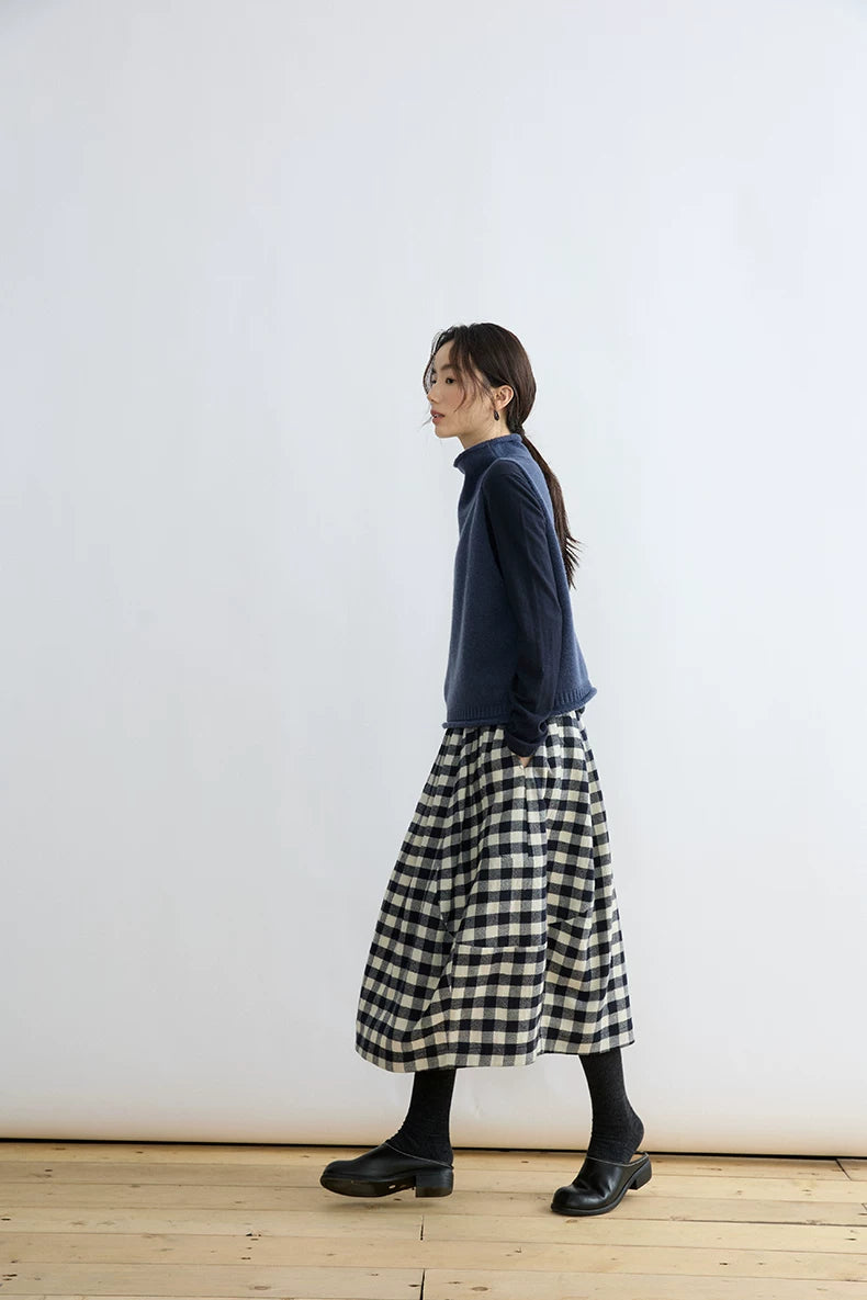 Side view of woman walking in Ink Blue wool mock-neck sweater vest layered over a long-sleeve top