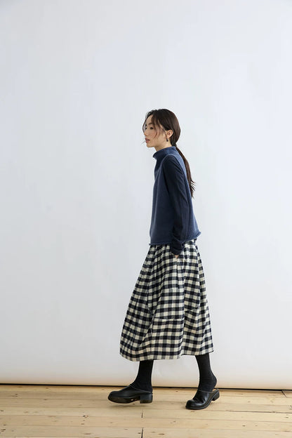 Side view of woman walking in Ink Blue wool mock-neck sweater vest layered over a long-sleeve top