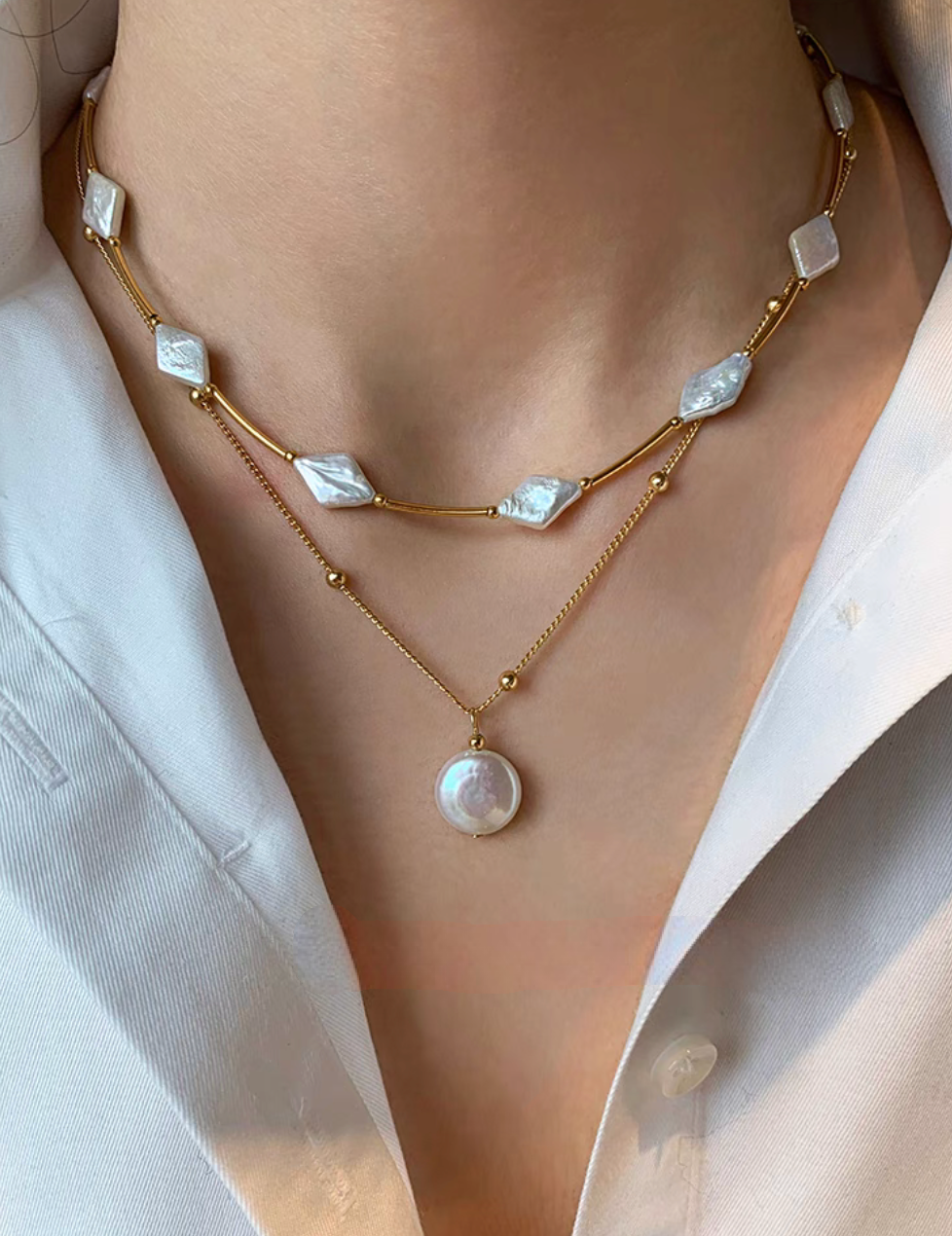 Layered look of irregular baroque pearl necklace with diamond-shaped pearls paired with gold chain pendant necklace worn on neck