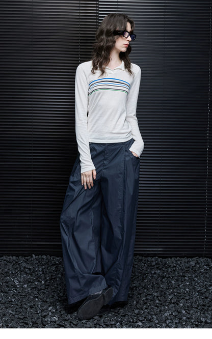 Model leaning against a wall in Ivory Stripe cotton-cashmere polo sweater and navy wide-leg pants