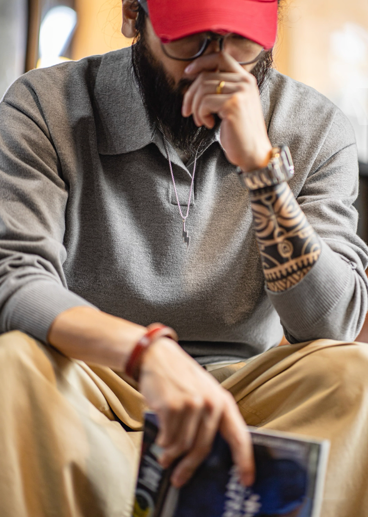 Model wearing gray knit polo sweater with red cap in casual indoor setting.