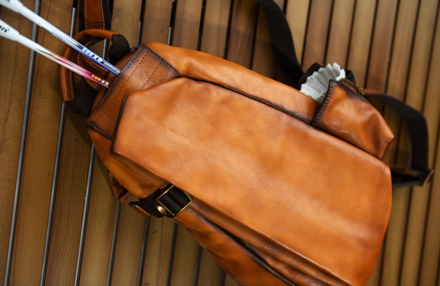 Camel brown leather sling bag, front view, single-strap backpack with side zip pocket.