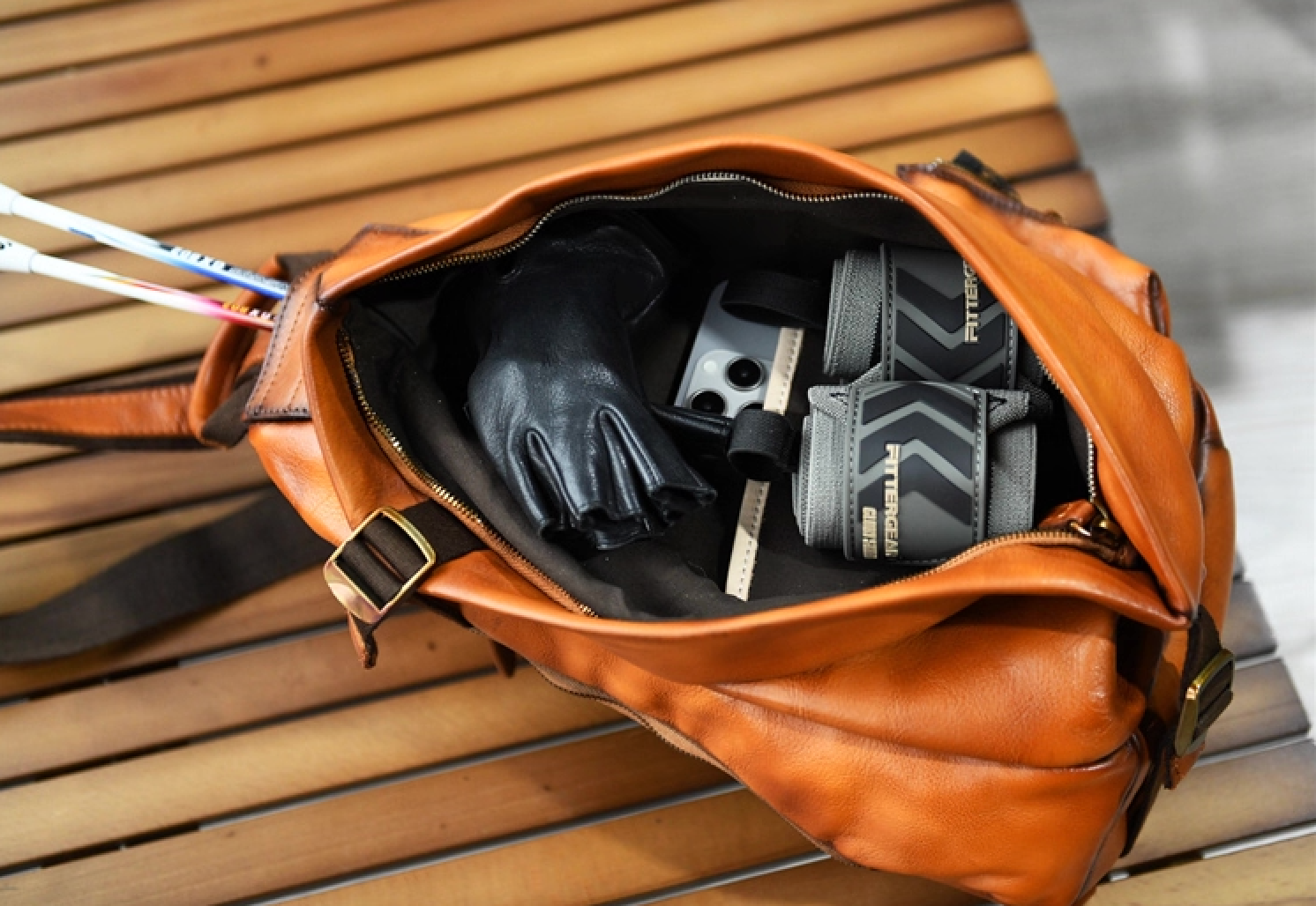 Open camel brown leather sling bag displaying roomy main compartment with sports gear.