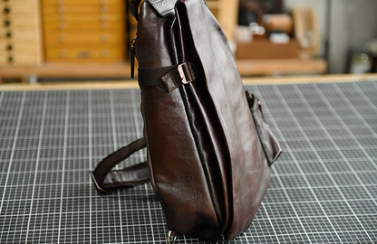 Side view of dark brown leather sling bag with folded body and adjustable strap.