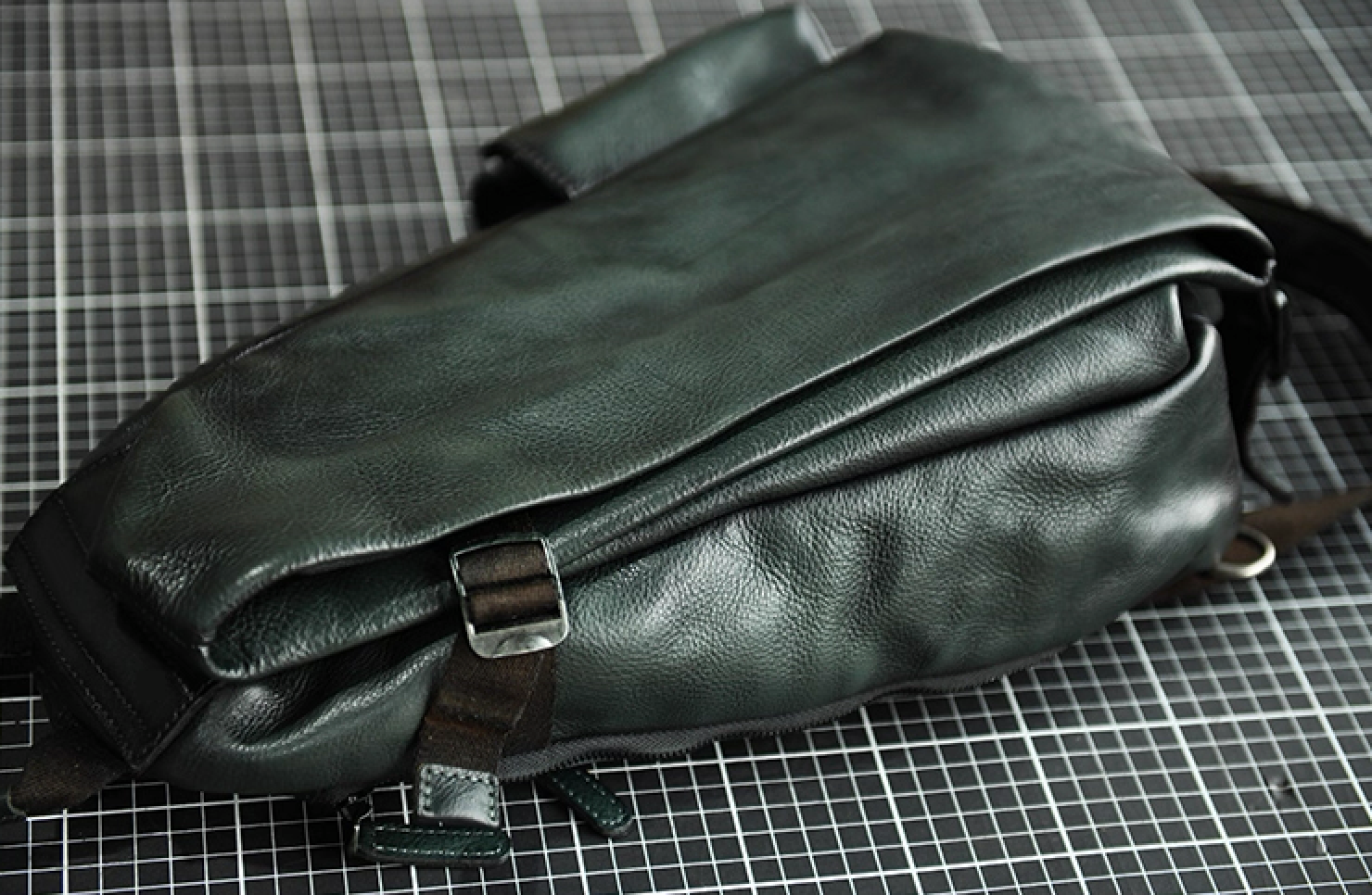Olive green leather sling bag laid flat, highlighting layered leather body and strap attachment.