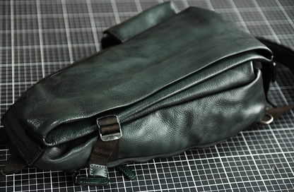 Olive green leather sling bag laid flat, highlighting layered leather body and strap attachment.
