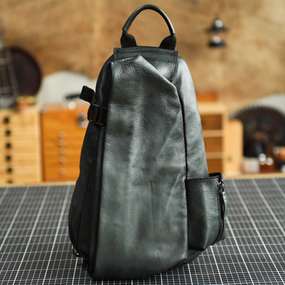 Olive green leather sling bag front view on worktable with top handle and side pocket.