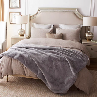 Light gray reversible faux fur throw blanket spread across bed in a luxury bedroom setting