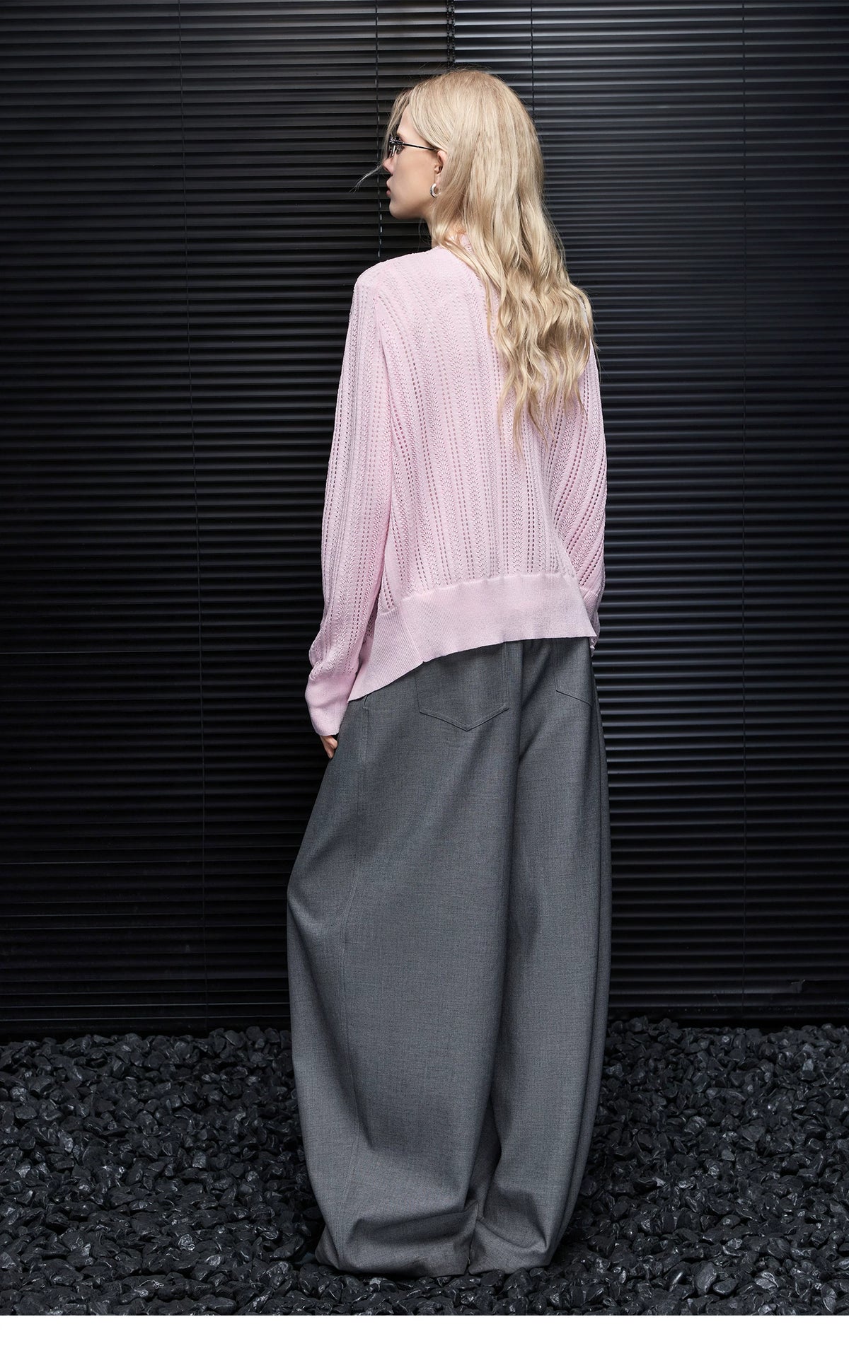 Back view of Light Pink pointelle cardigan showing raglan sleeves and banded hem with grey wide-leg trousers