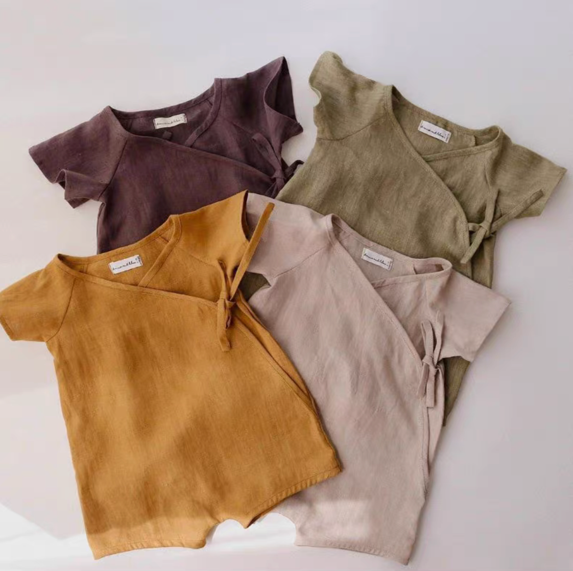 Assorted cotton muslin baby rompers in multiple colors laid flat together