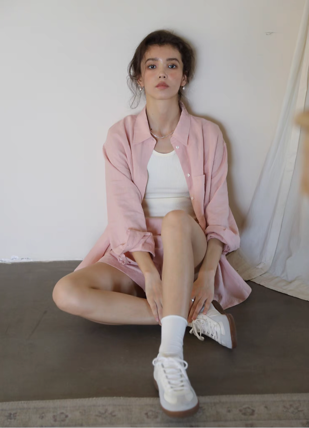Pink linen shirt and shorts set sitting pose relaxed casual styling with sneakers