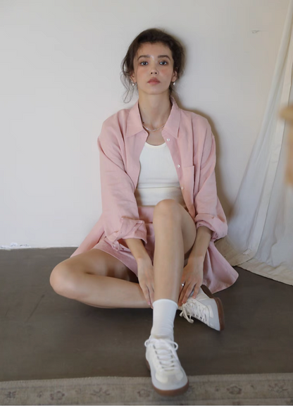 Pink linen shirt and shorts set sitting pose relaxed casual styling with sneakers