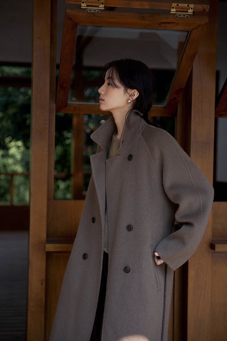 Woman in coffee brown double-faced llama wool coat standing sideways in a wooden doorway