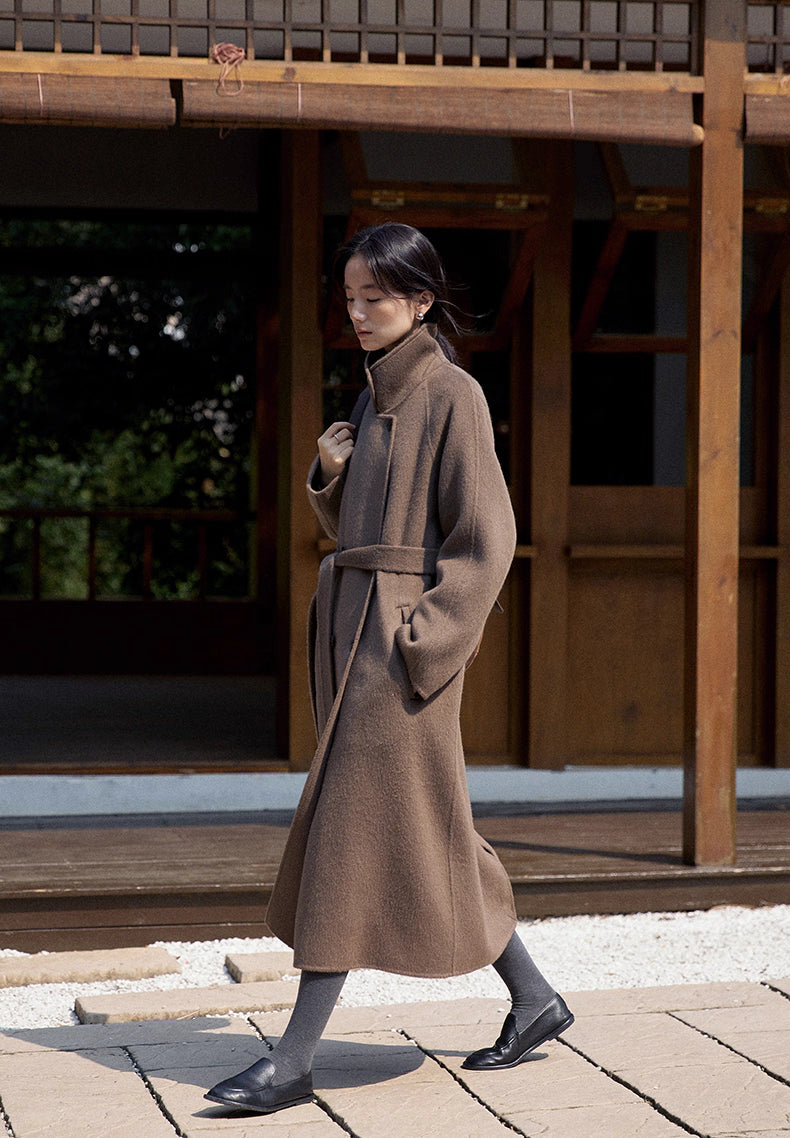 Full body shot of woman walking outdoors in a long belted llama wool coat