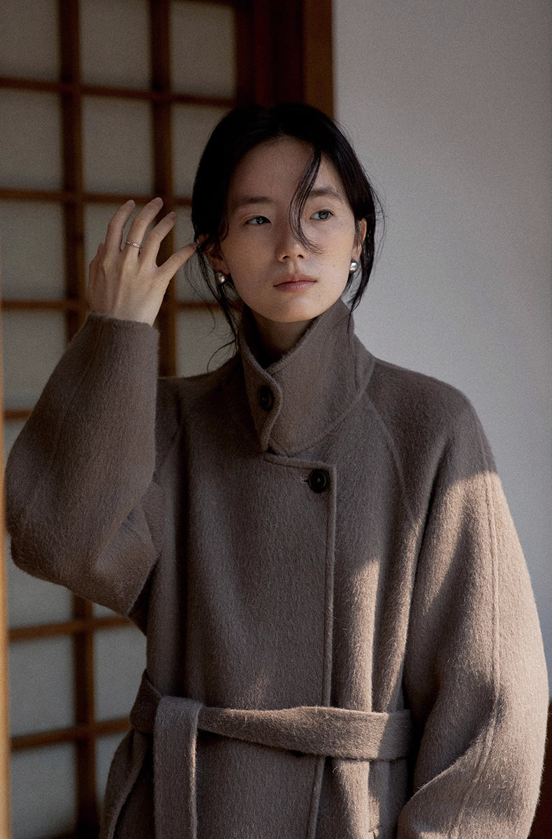 Portrait of woman wearing stand-collar llama wool coat with belt tied at the waist