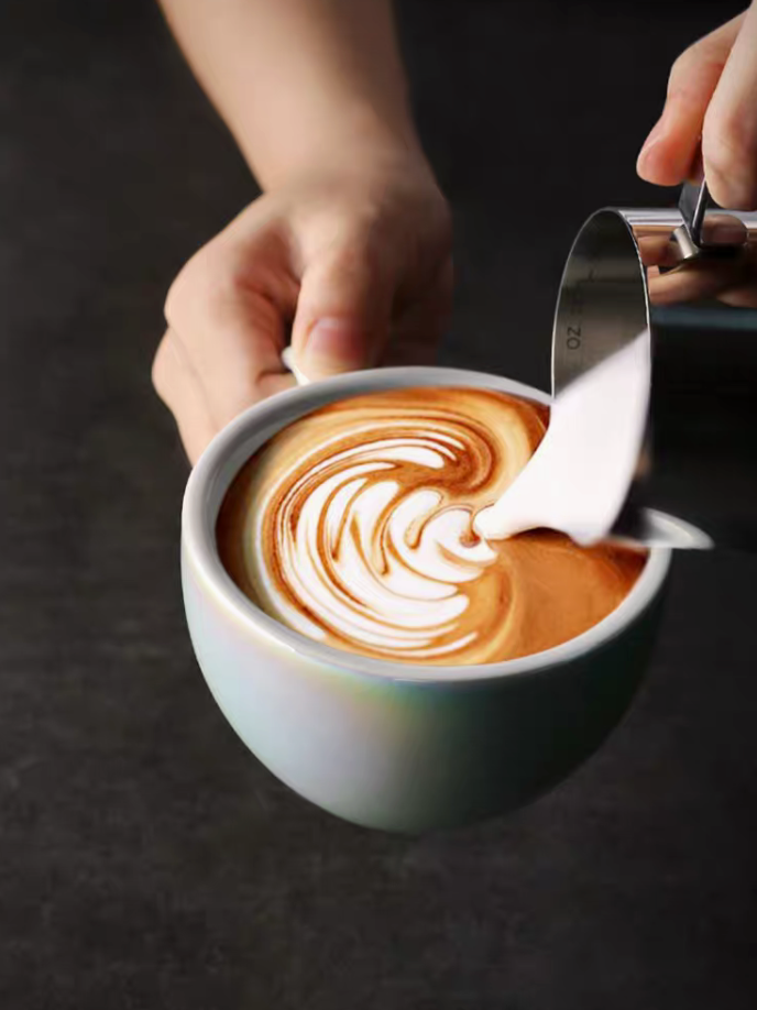 Luminous iridescent blue ceramic coffee cup with milk pouring into espresso creating latte art swirl detail
