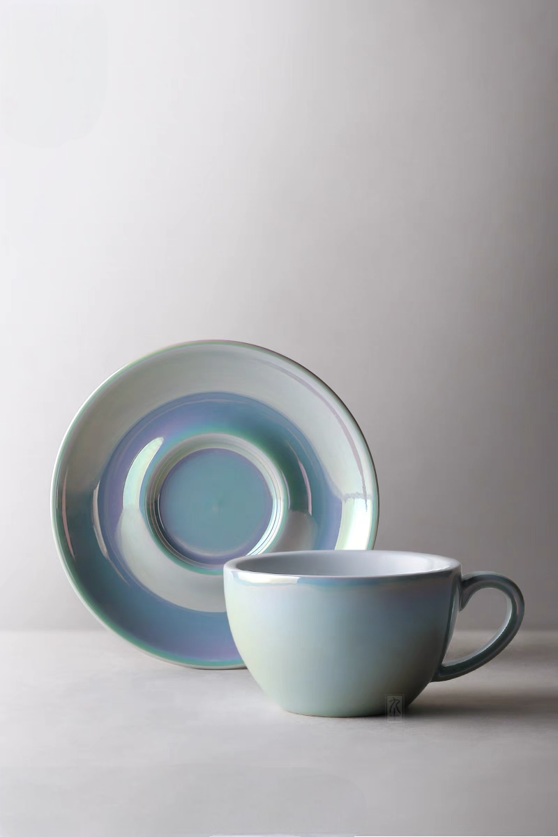 Luminous iridescent blue ceramic coffee cup and saucer set in front view with glossy pearl-like finish and smooth minimalist design