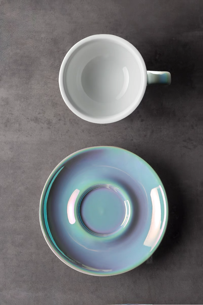 Top view of luminous iridescent blue ceramic coffee cup and saucer highlighting glossy interior and reflective glaze finish