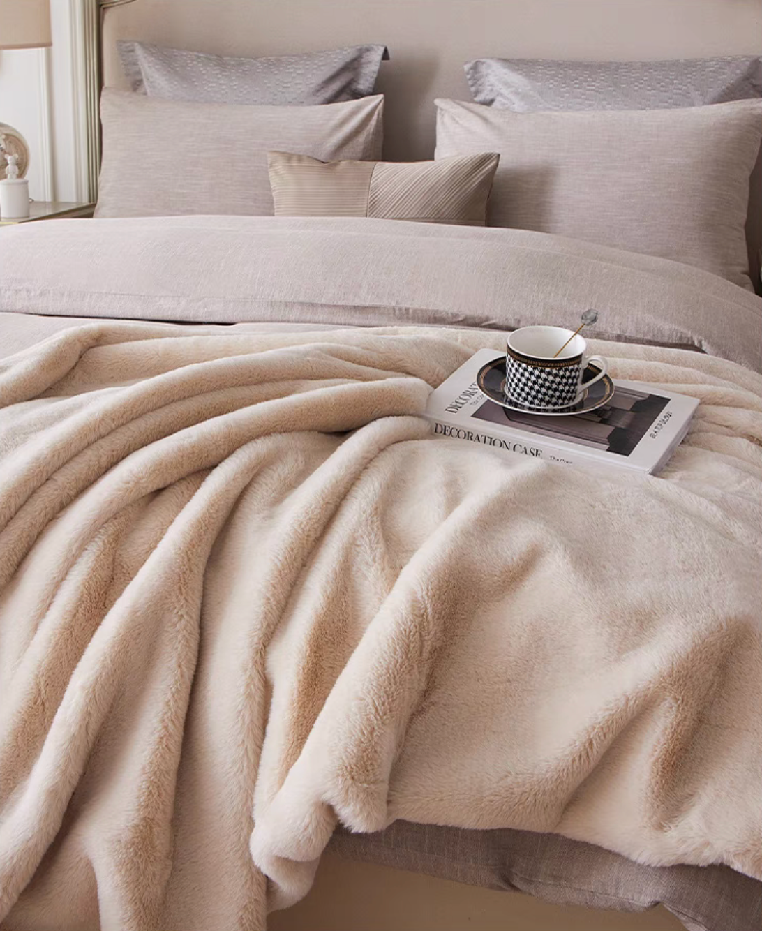 Soft beige faux fur throw blanket styled on bed with decorative pillows for a warm bedroom look