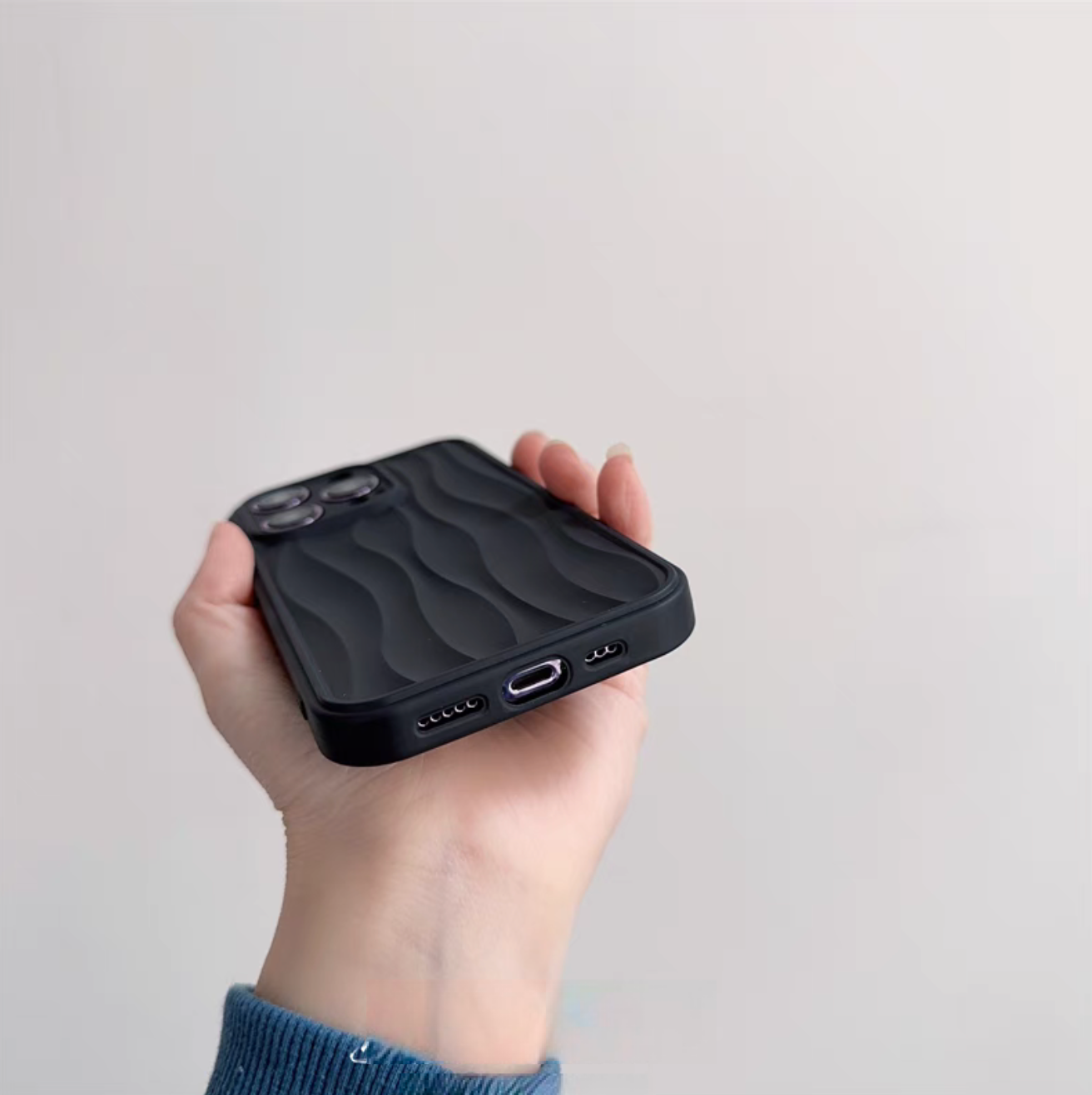 Matte black wave phone case showing bottom cutouts for charging port and speakers with textured wave design