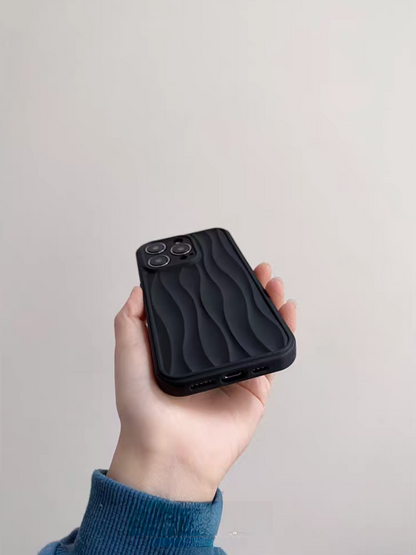 Matte black wave phone case held in hand from a lower angle showing textured surface and port openings