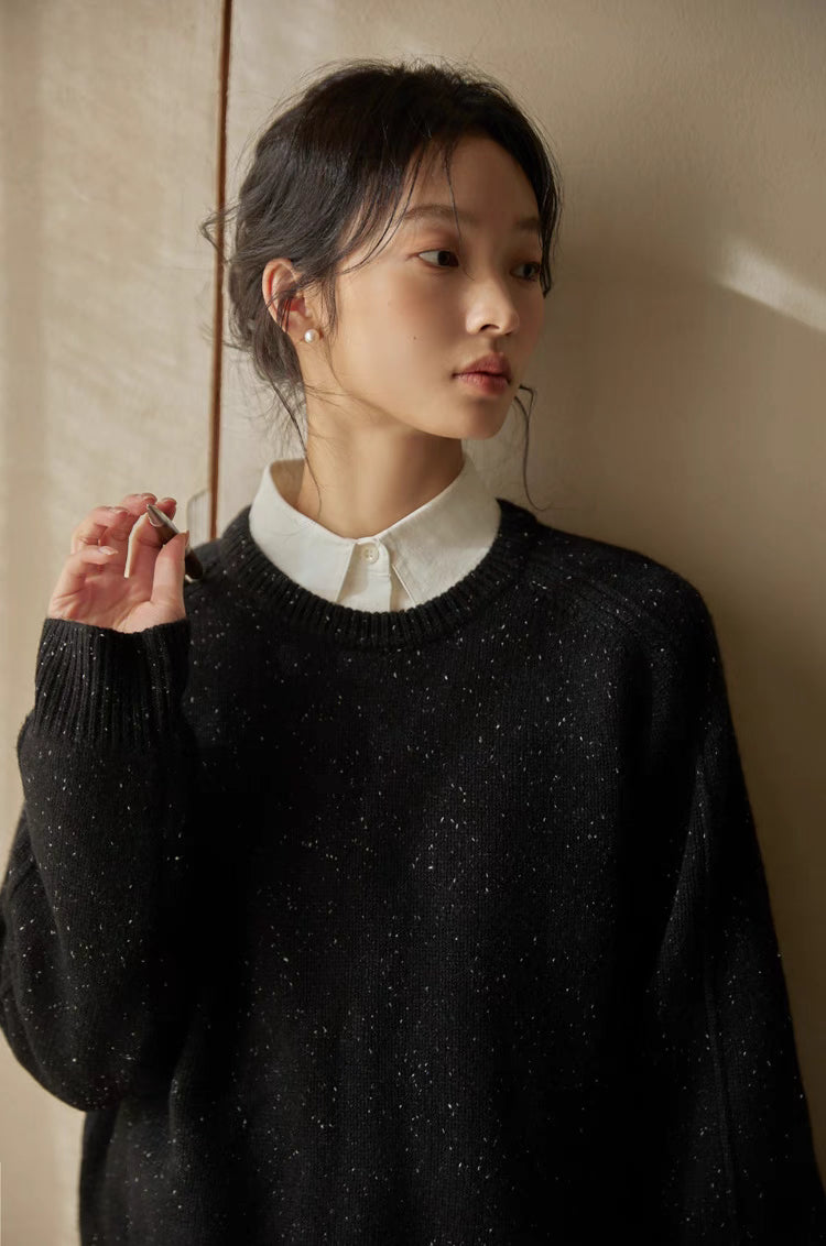 Black speckled merino wool sweater close-up with soft lighting emphasizing subtle fleck details and soft texture