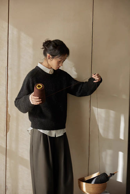 Black speckled merino wool sweater styled during yarn work moment highlighting cozy artisanal feel