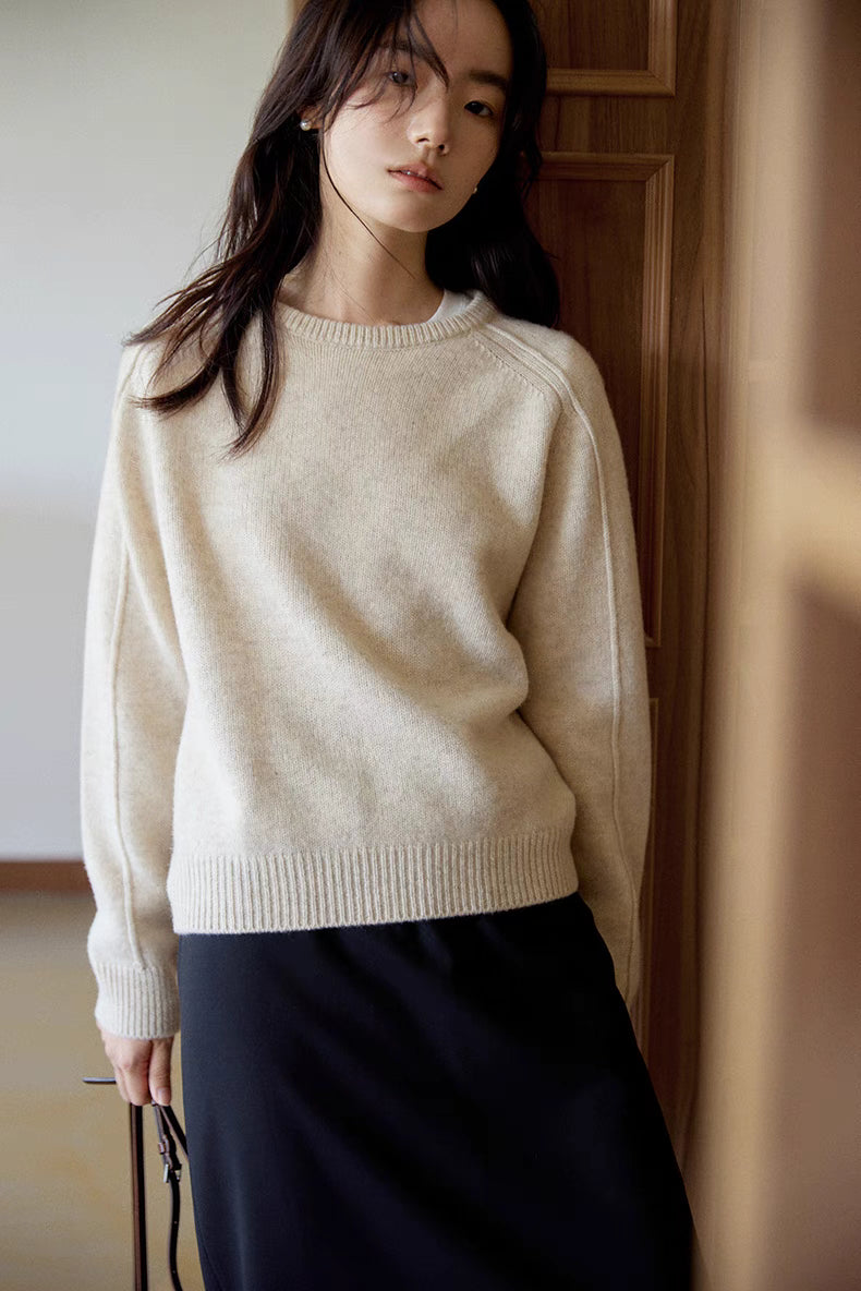 Mist white merino wool sweater worn while leaning by wooden door with soft natural light highlighting smooth knit texture