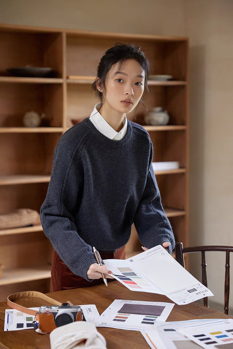 Shale gray merino wool sweater styled over white shirt while standing at table with design materials for a refined layered look