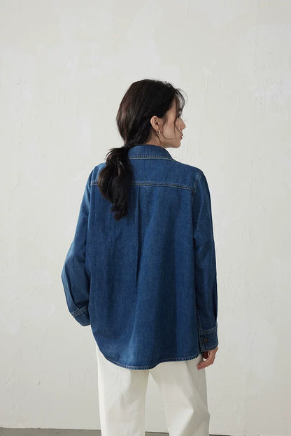 Back view of a medium blue denim shirt with a center back pleat and curved hem