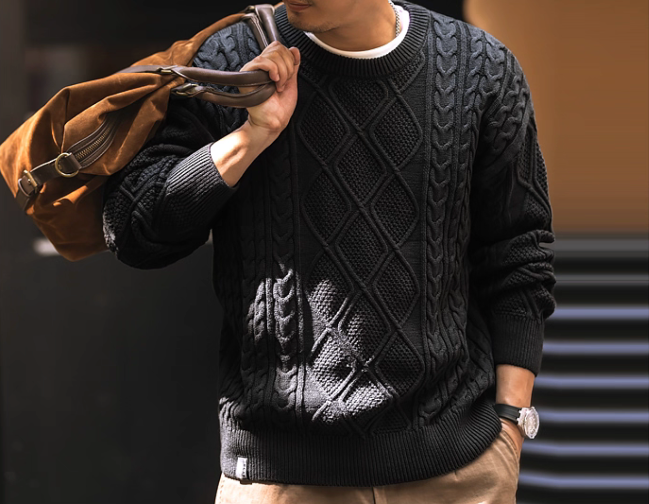 Lifestyle photo, men’s diamond cable knit sweater with leather bag.
