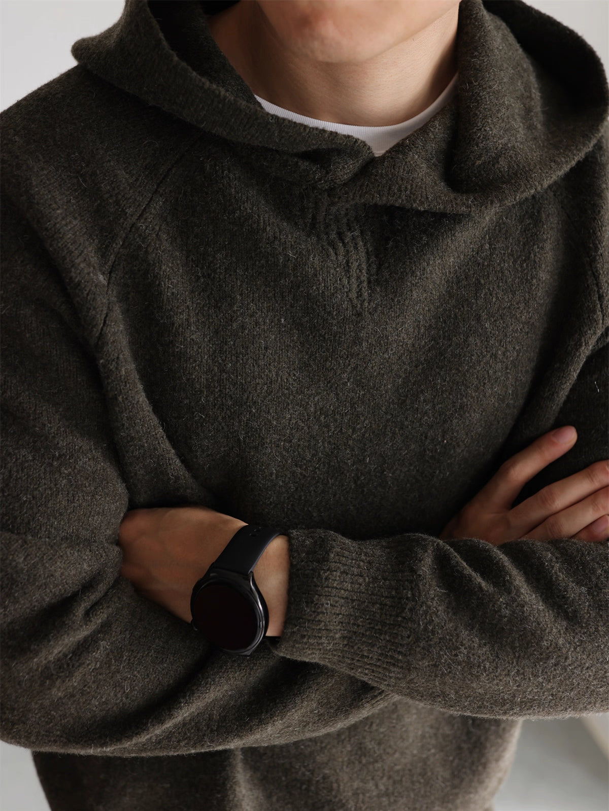 Minimalist olive knit hoodie, model crossing arms showing raglan sleeves