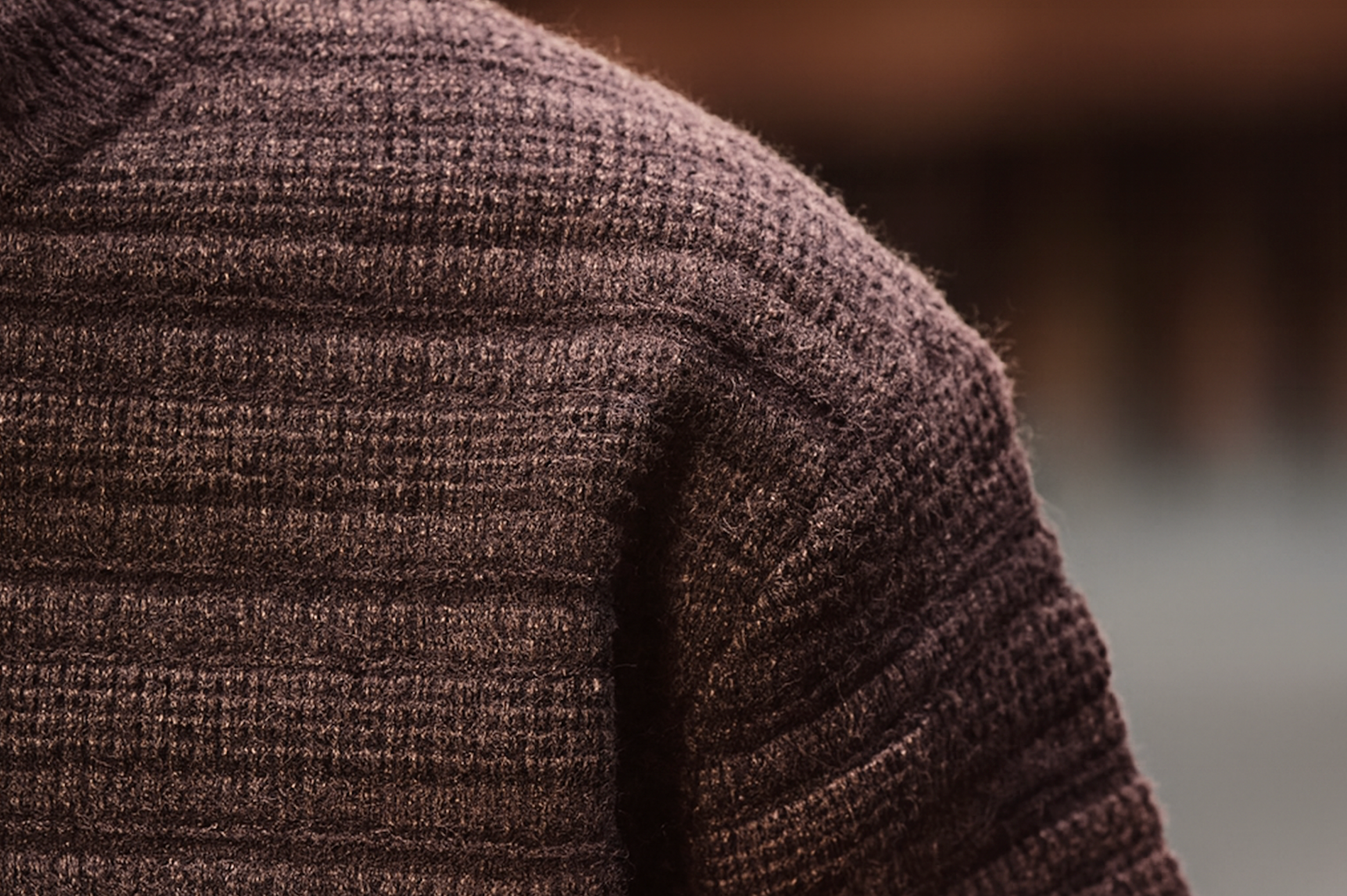 Close-up of shoulder detail on brown textured Henley knit sweater showing ribbed horizontal knit pattern.