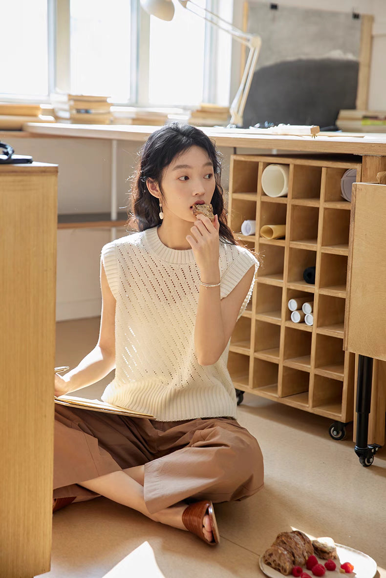Model wearing Camellia White openwork knit top sitting on floor in sunlit studio, showcasing breathable texture, cap sleeves, and relaxed lifestyle styling
