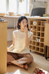 Model wearing Camellia White openwork knit top sitting on floor in sunlit studio, showcasing breathable texture, cap sleeves, and relaxed lifestyle styling