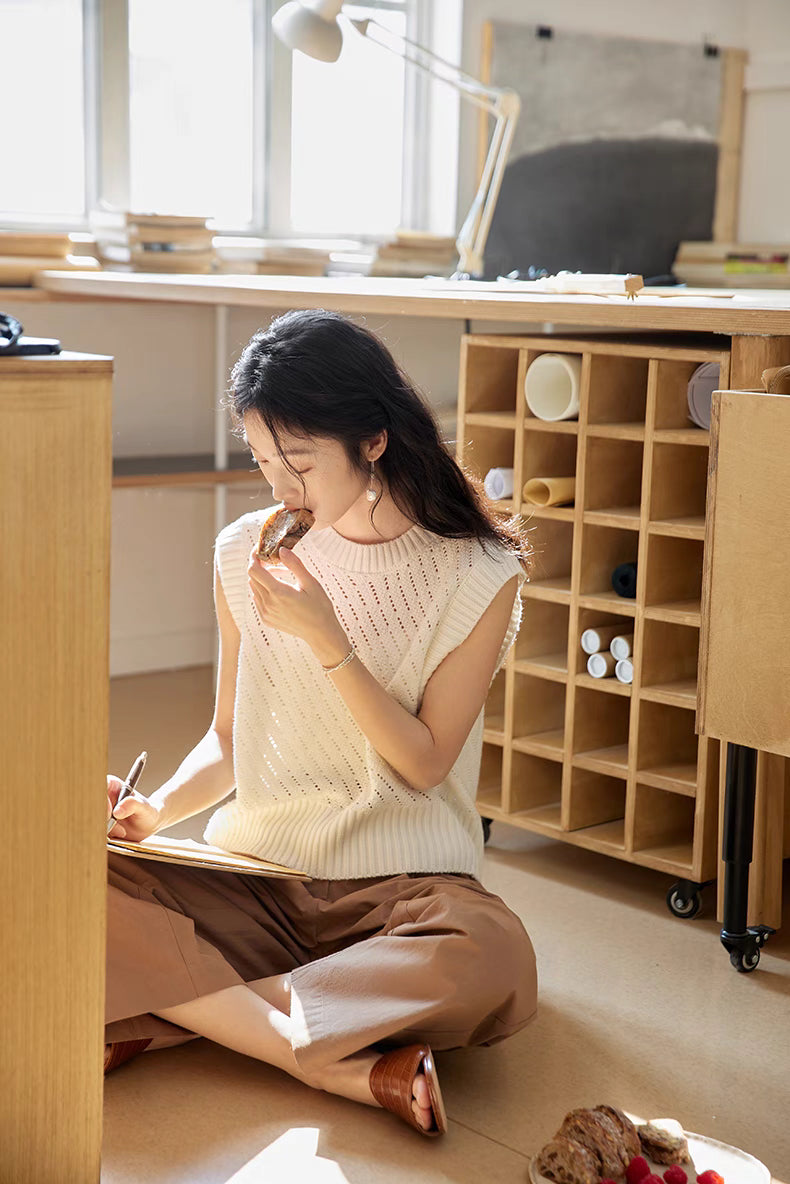 Camellia White openwork knit vest styled in creative studio setting with model sketching, highlighting lightweight knit, soft sheen, and comfortable fit