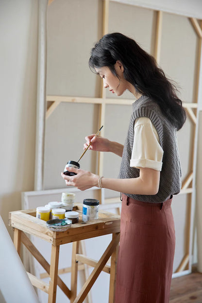 Side close-up of Cool Black Tea openwork knit top during painting activity, highlighting soft texture, cap sleeves, and refined craftsmanship