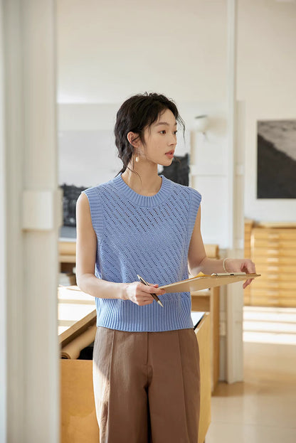 Model wearing Misty Blue openwork knit top holding clipboard, showcasing refined knit pattern, cap sleeves, and polished minimalist look