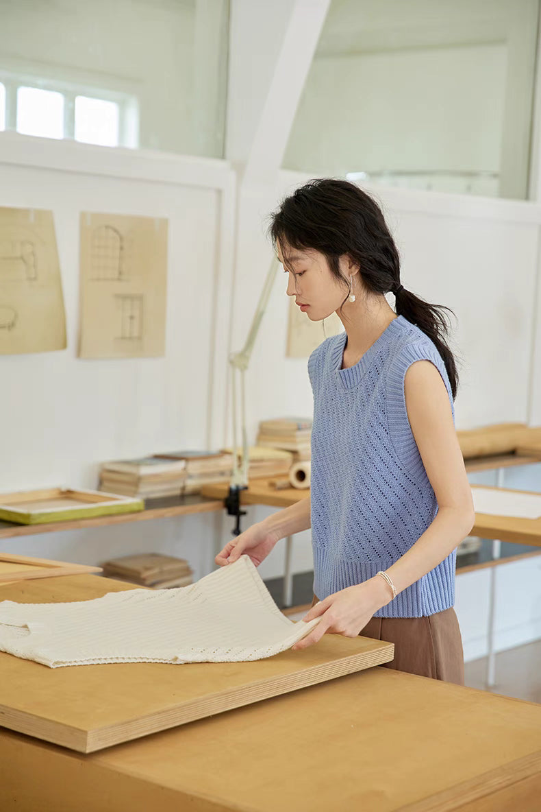 Side view of Misty Blue knit top in workspace setting, highlighting breathable openwork design, soft drape, and lightweight fabric texture