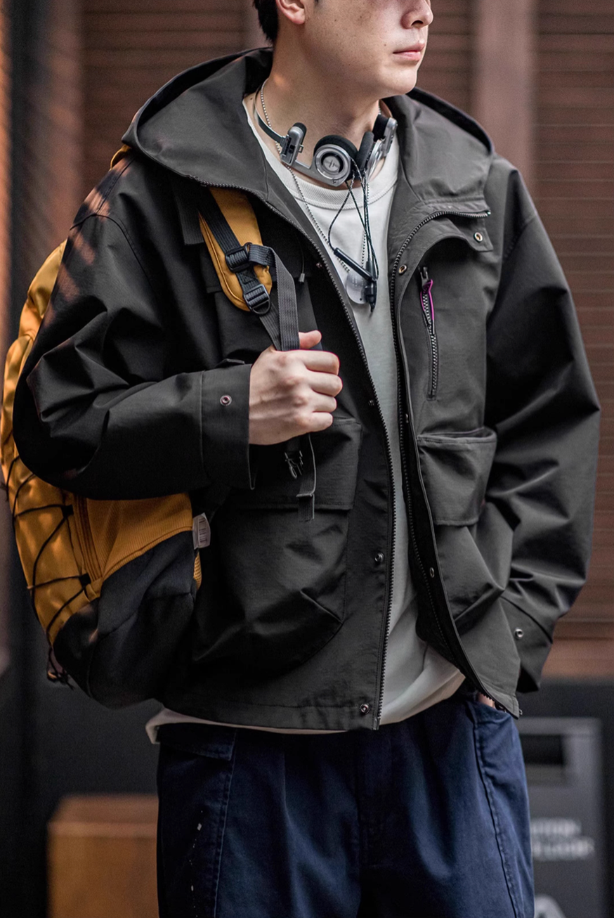 Man wearing Black Metro Flex Waterproof Jacket with backpack showing front zip closure, utility pocket layout and outdoor styling