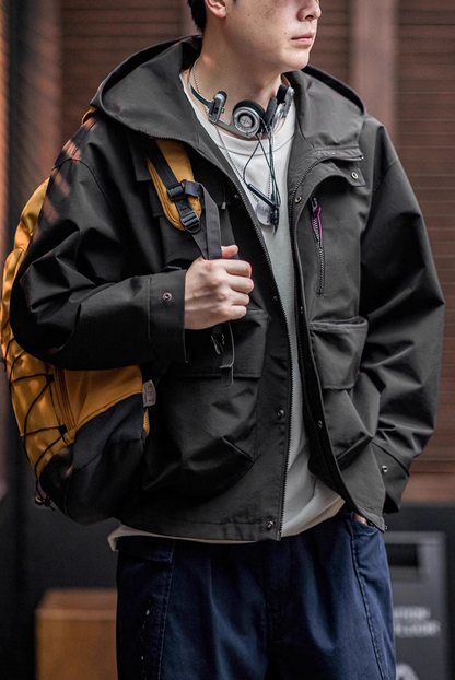 Man wearing Black Metro Flex Waterproof Jacket with backpack showing front zip closure, utility pocket layout and outdoor styling