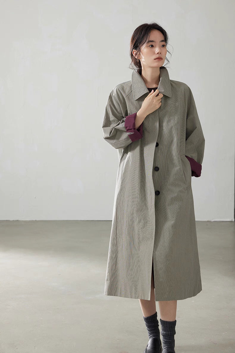 Front view of model wearing light khaki gray relaxed-fit cotton trench coat with burgundy cuffs and mid-long length.