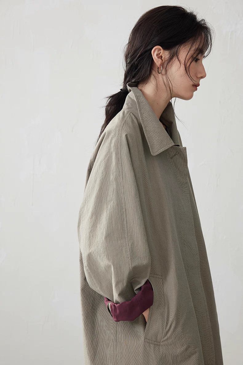 Side profile of model in light khaki gray trench coat with rolled burgundy cuff and relaxed sleeve shape.