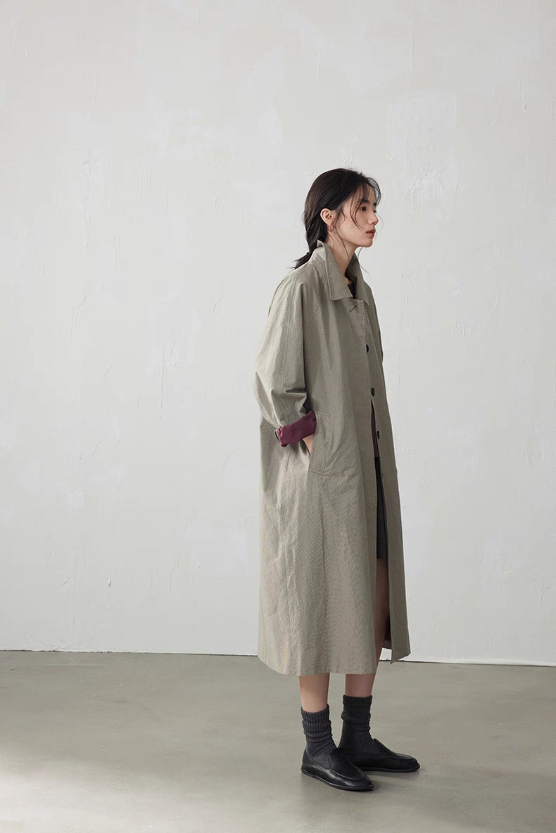 Full side view of light khaki gray long cotton trench coat, straight fit falling to mid-calf.
