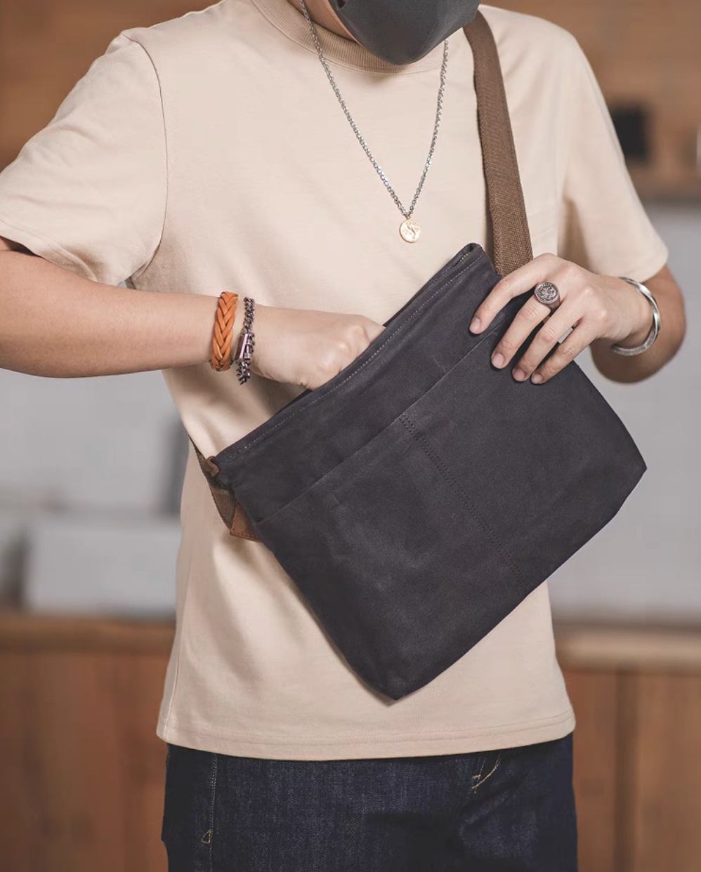 Model wearing dark grey waxed canvas crossbody bag across the body, showing practical everyday use and adjustable strap fit.