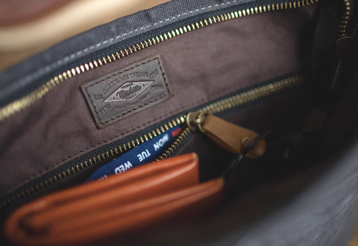 Close-up of the interior of the dark grey waxed canvas crossbody bag showing zippered pocket, leather label, and organized compartments.